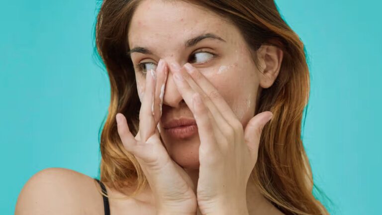 A woman covers her eyes with cream, her hands positioned delicately over her face.