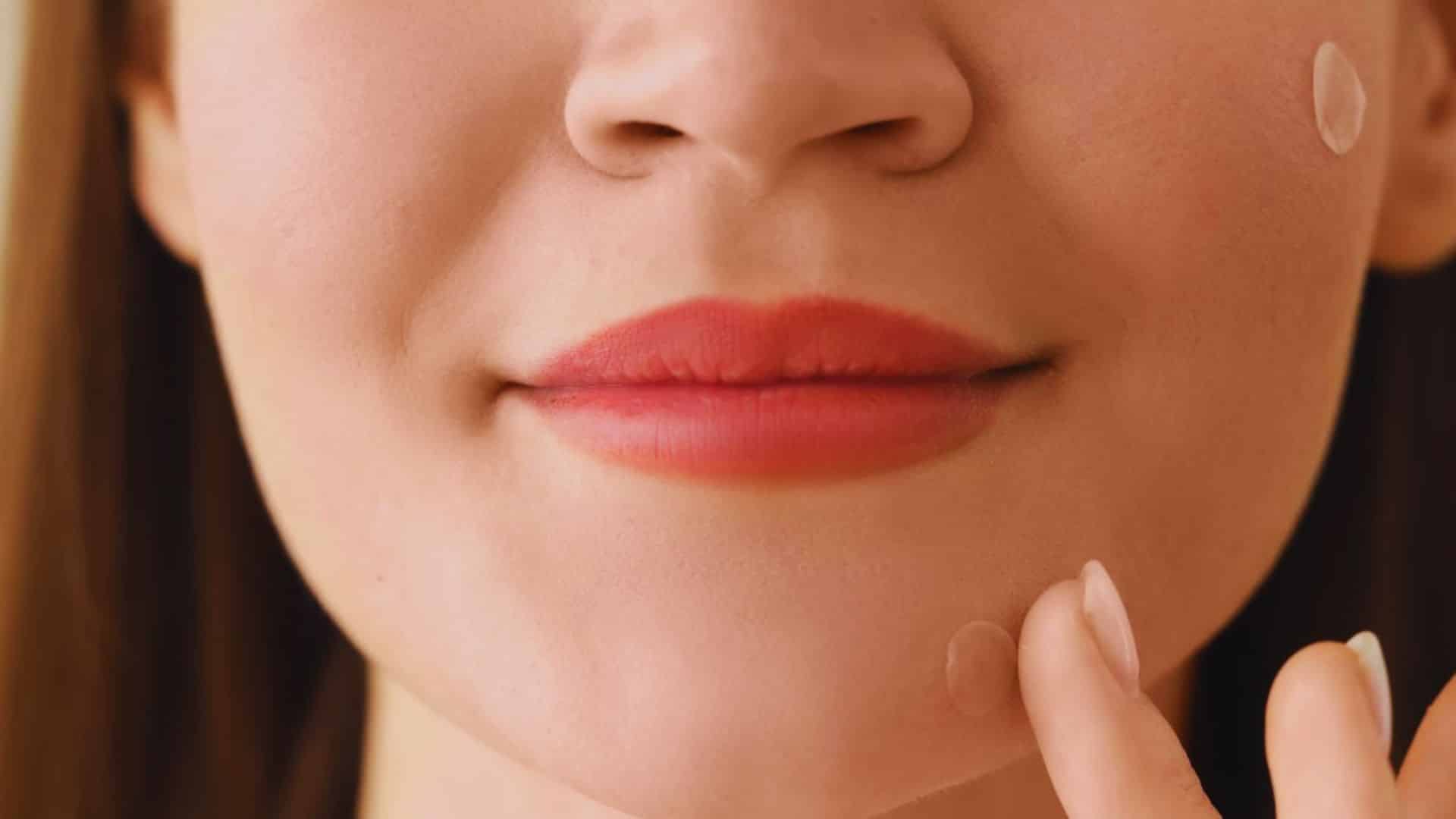 A woman applies lip cream, gently smoothing it over her lips with her fingertip.