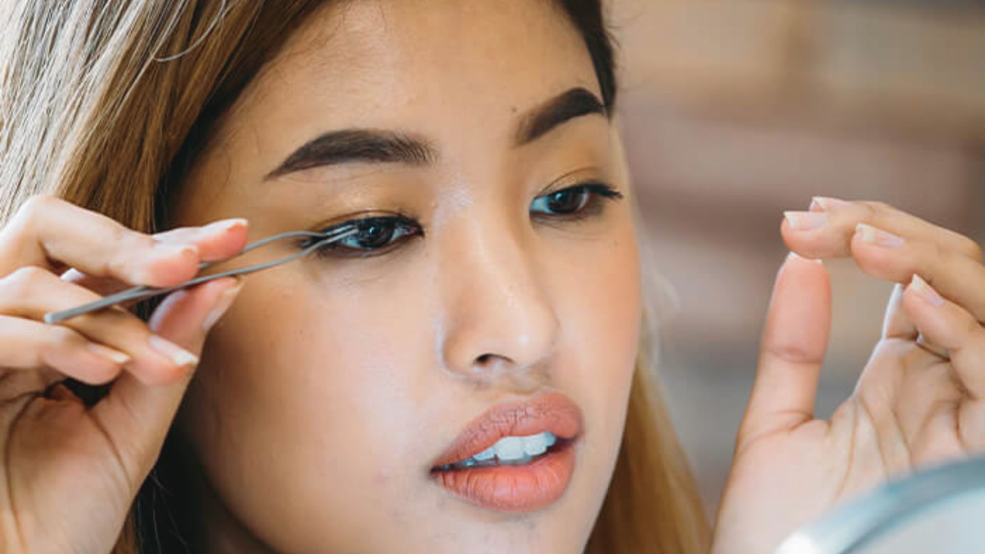 A woman examines her eyelashes closely while holding a pair of scissors in her hand.