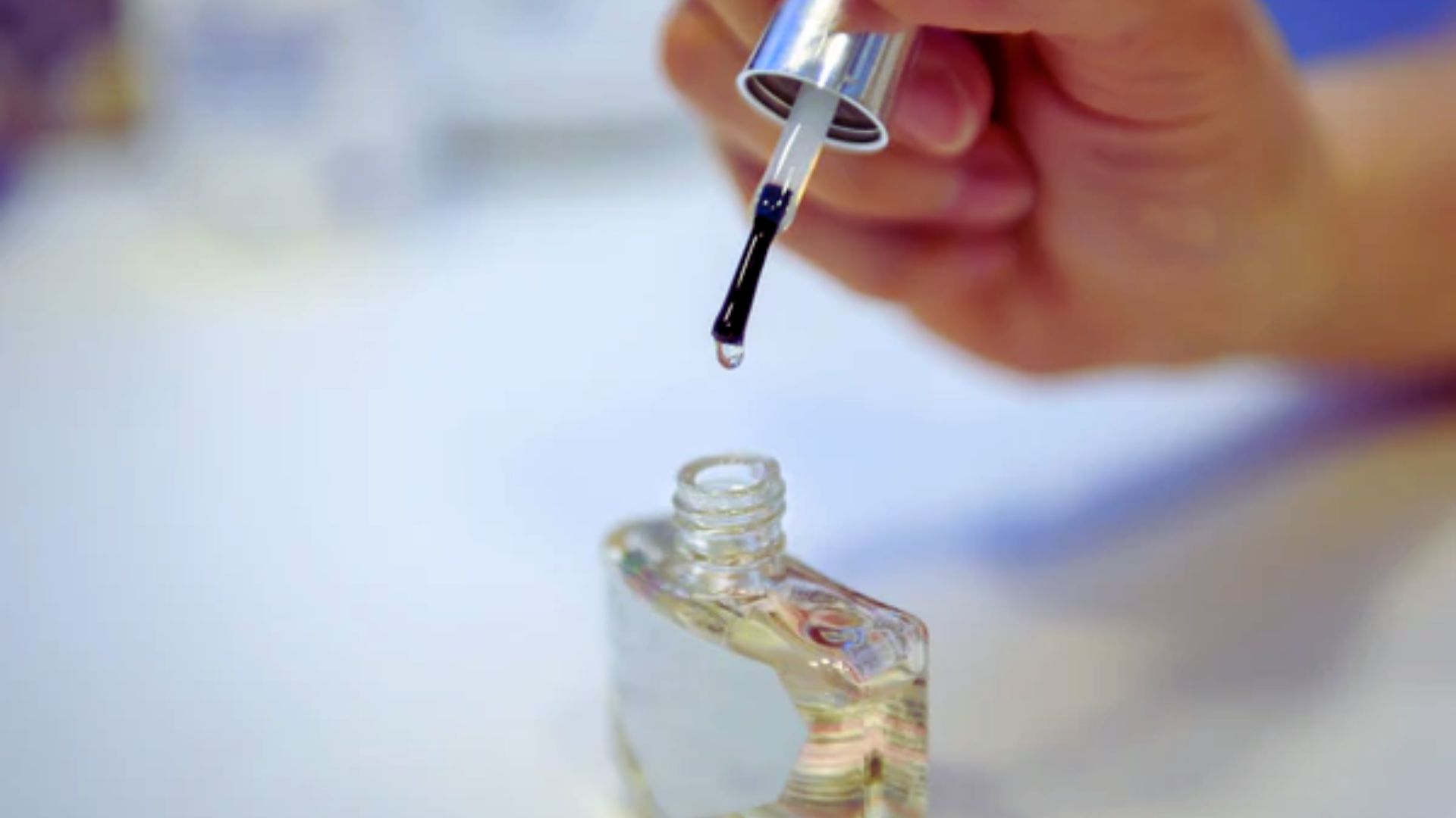 A person holds a bottle of nail polish, showcasing a vibrant color against a neutral background.