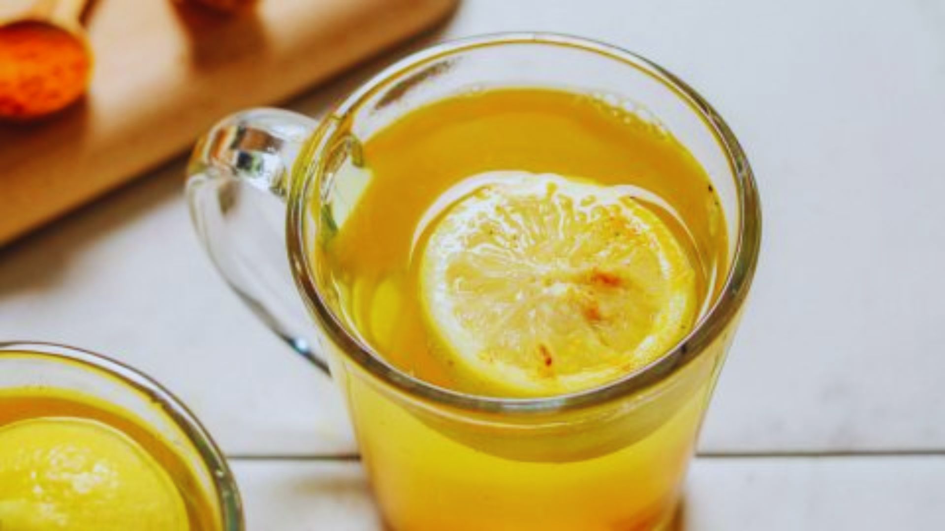Two glasses of lemon tea, each garnished with a slice of lemon, placed on a wooden table.