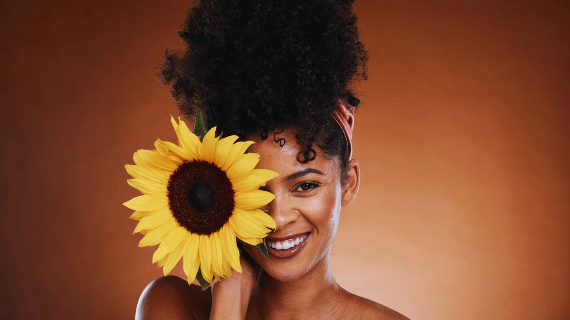 A woman stands with a sunflower in her hand, radiating joy and appreciation for nature's beauty.