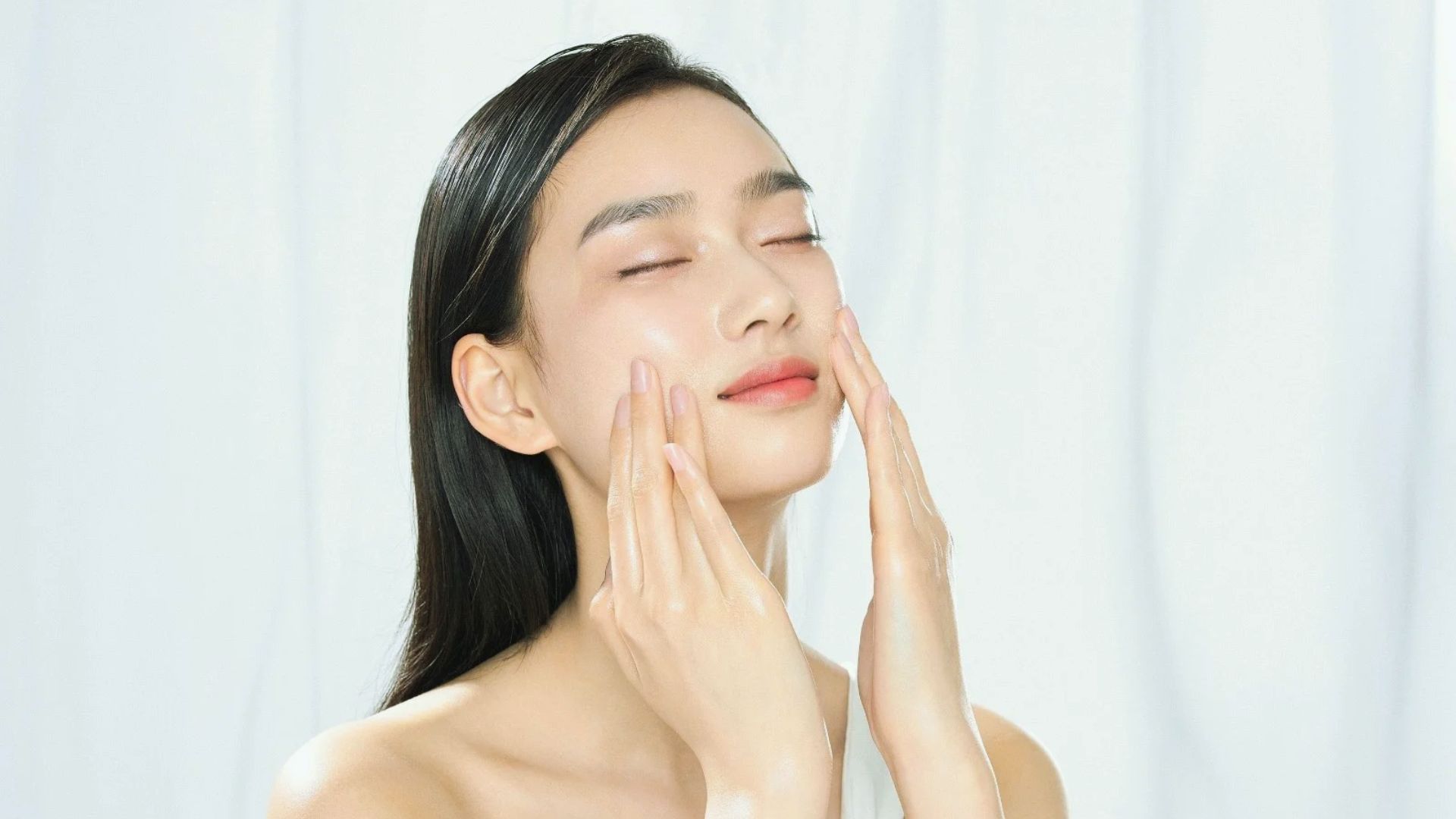 A woman applies a facial mask to her face, focusing on skincare and self-care in a bright, well-lit room.