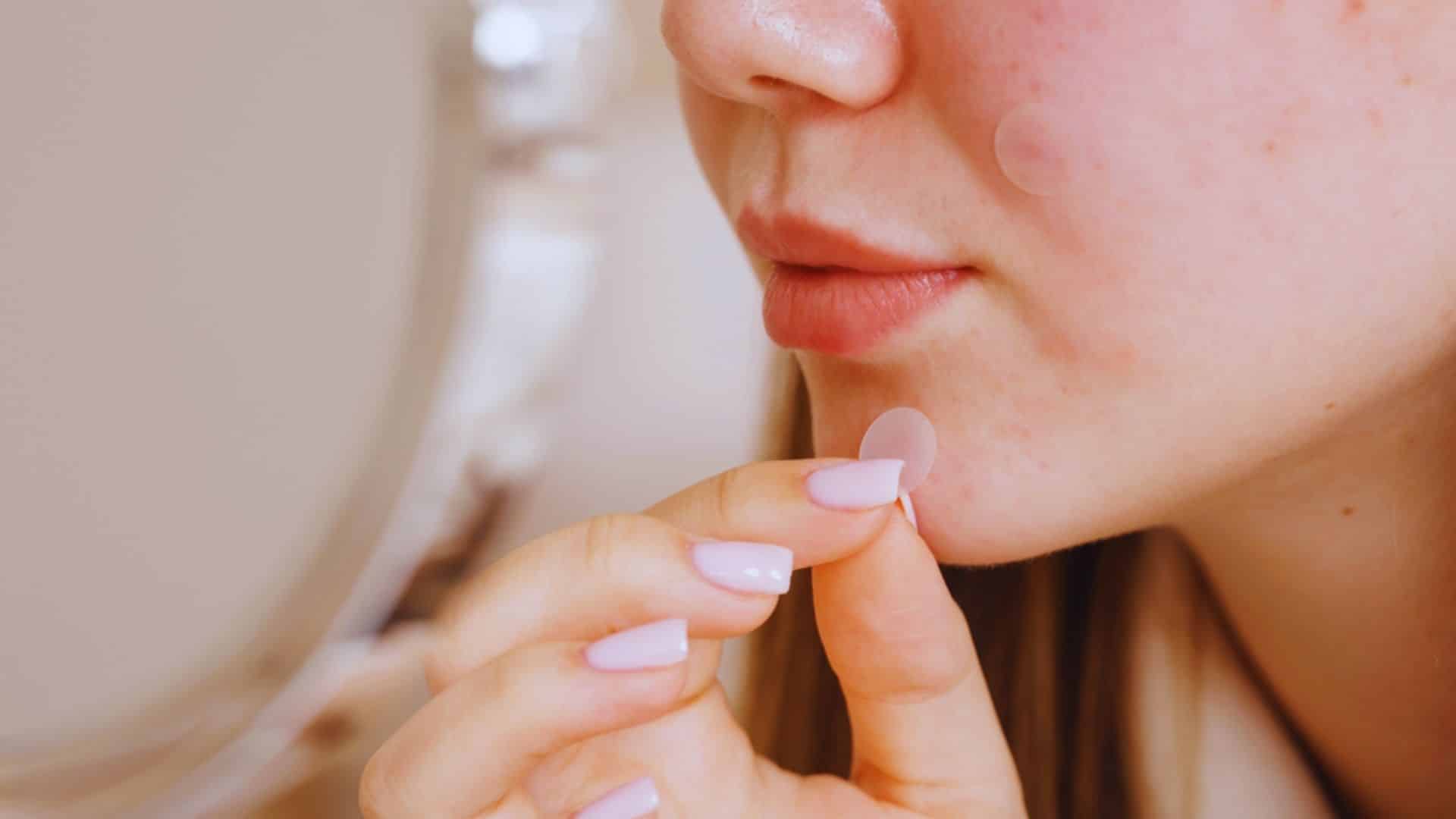 A woman with pink nails gazes at her reflection in a mirror, examining her face closely.