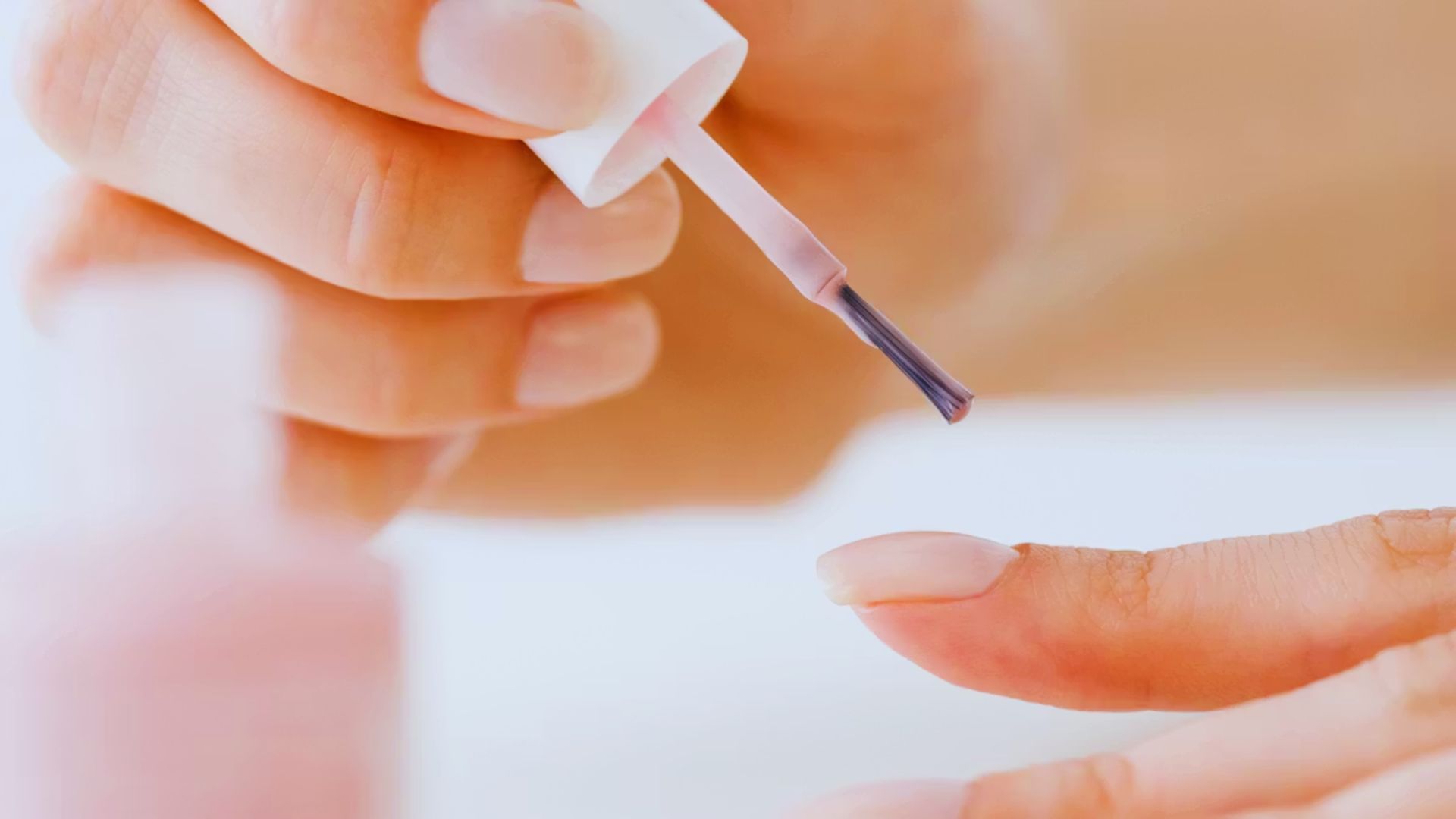A person carefully applies bright red nail polish to their fingernail, showcasing a steady hand and attention to detail.