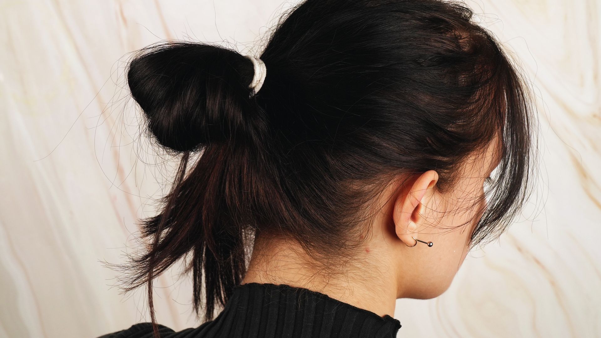 A woman wearing a black sweater and sporting a messy bun hairstyle.
