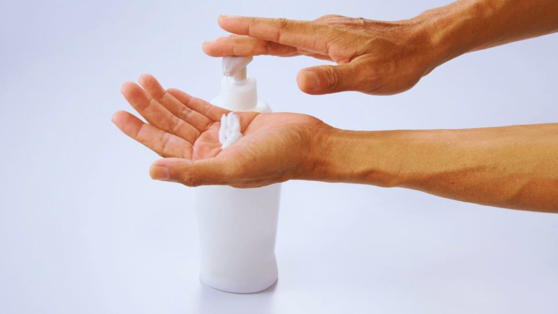 A woman in a towel applies cream to her face while holding her cheeks, focusing on her skincare routine.
