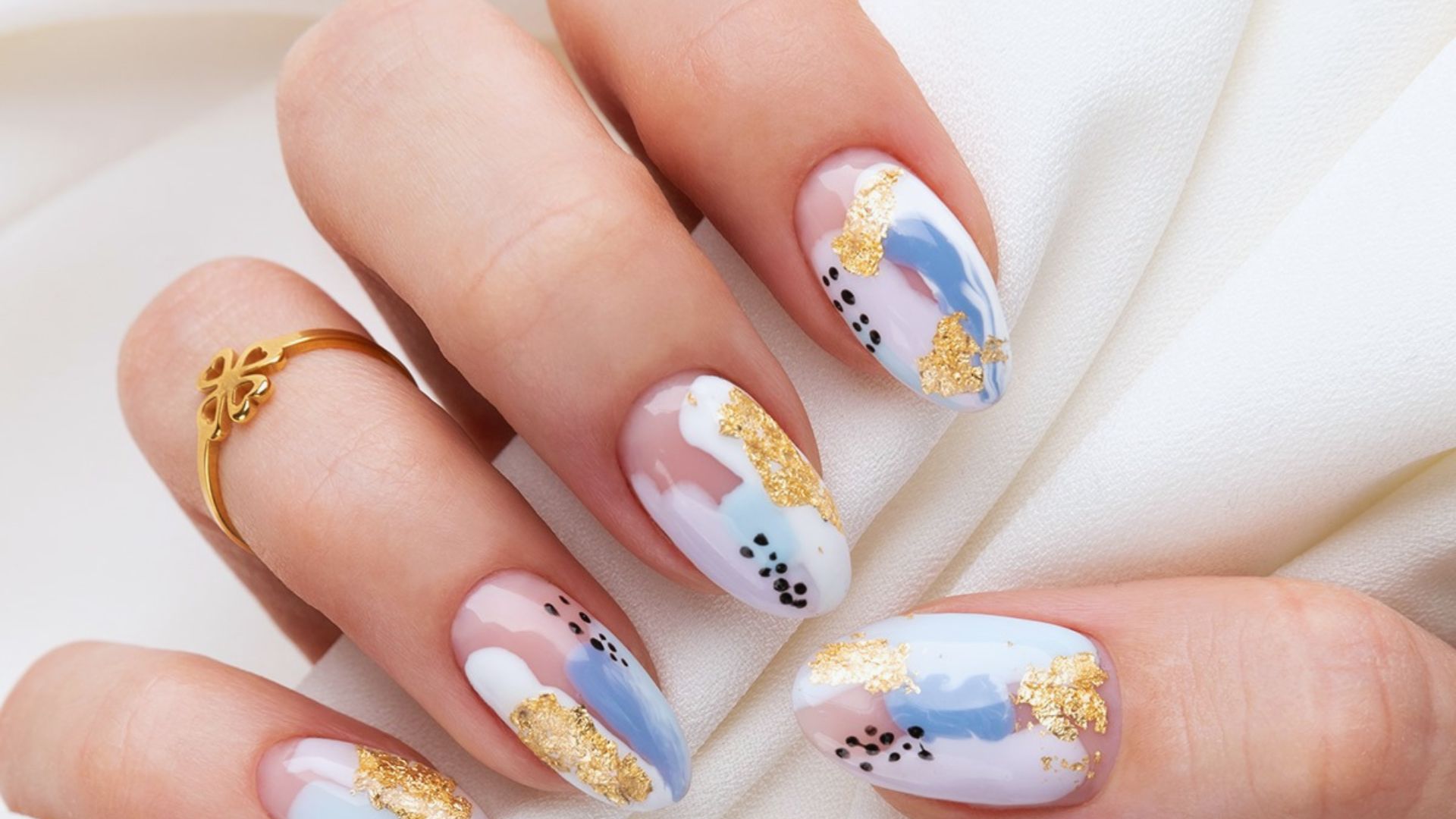 A close-up of a woman's hand showcasing a gold and blue manicure with intricate designs on the nails.