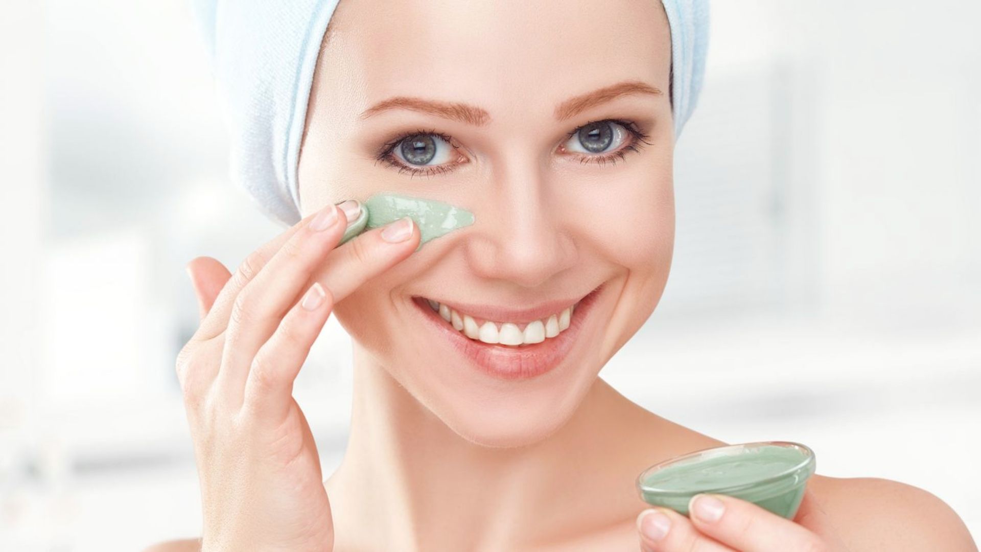 A woman holding a green face mask, preparing to apply it to her face for skincare.