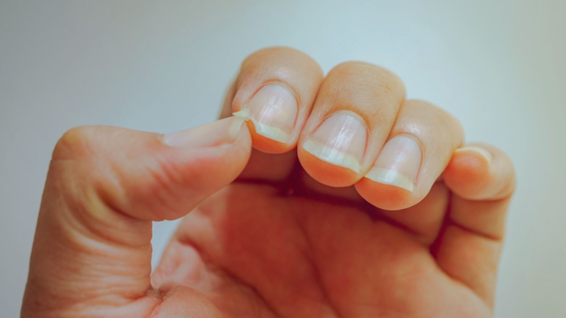 A person holding a nail file next to a freshly manicured nail, demonstrating nail care techniques.