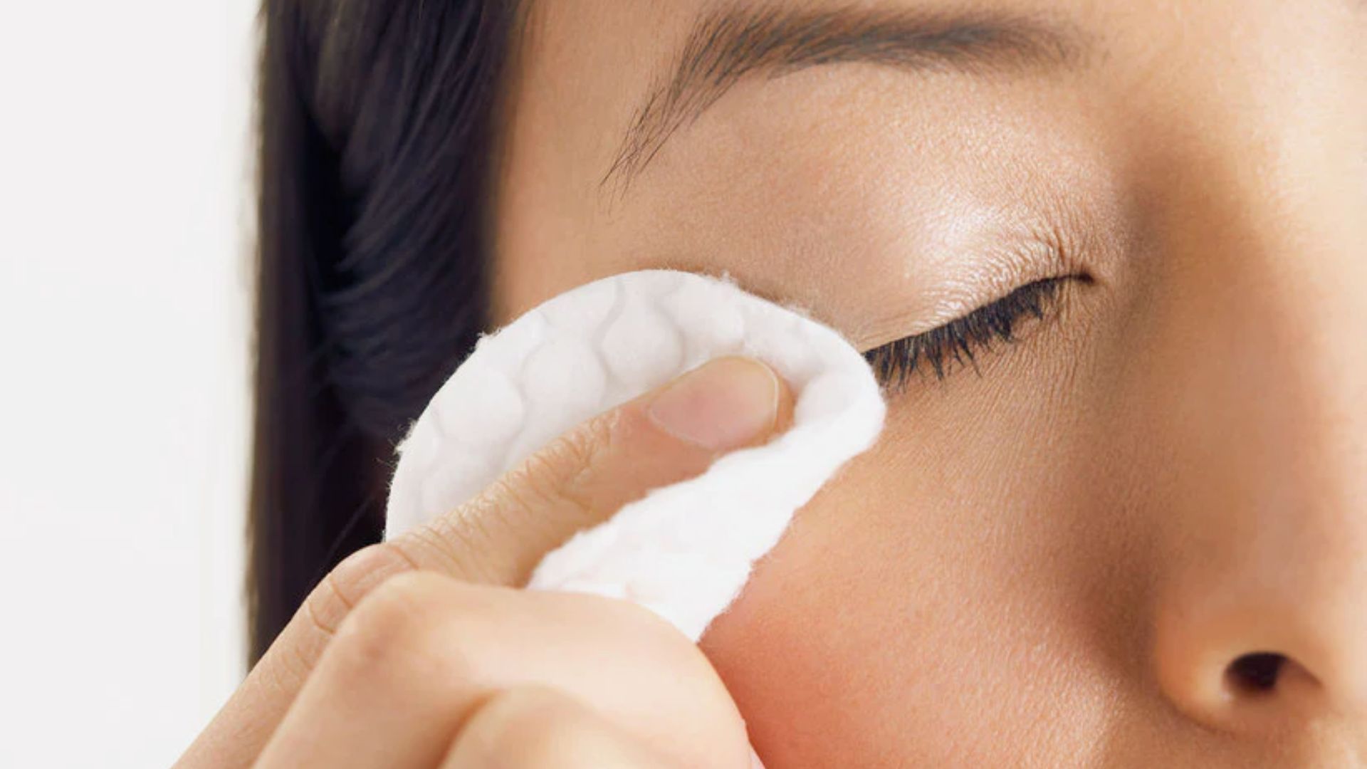 A woman gently cleans her eyes with a cotton pad, focusing on her skincare routine.