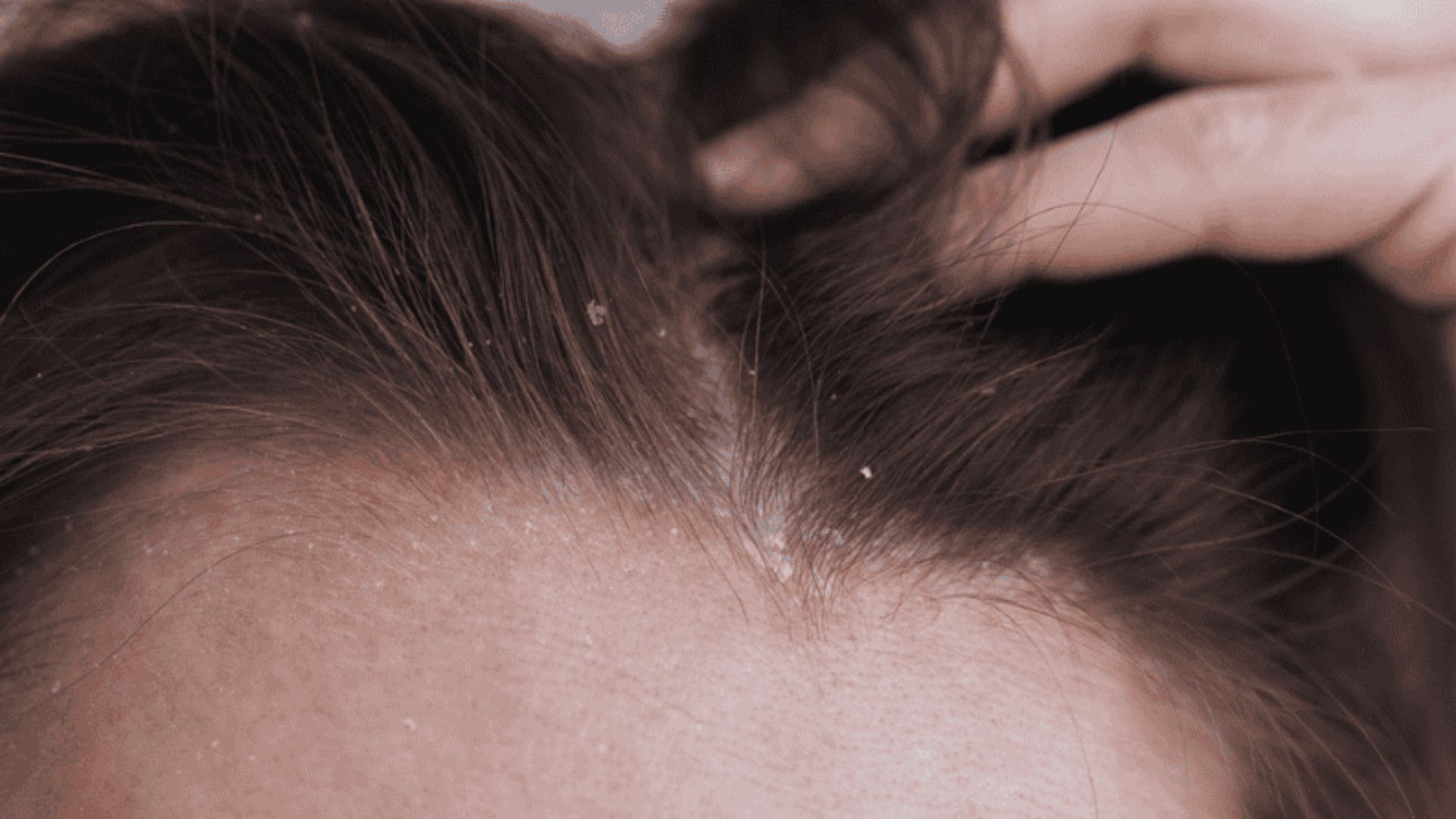 A woman is using a comb to style her hair, focusing on her reflection in a mirror.