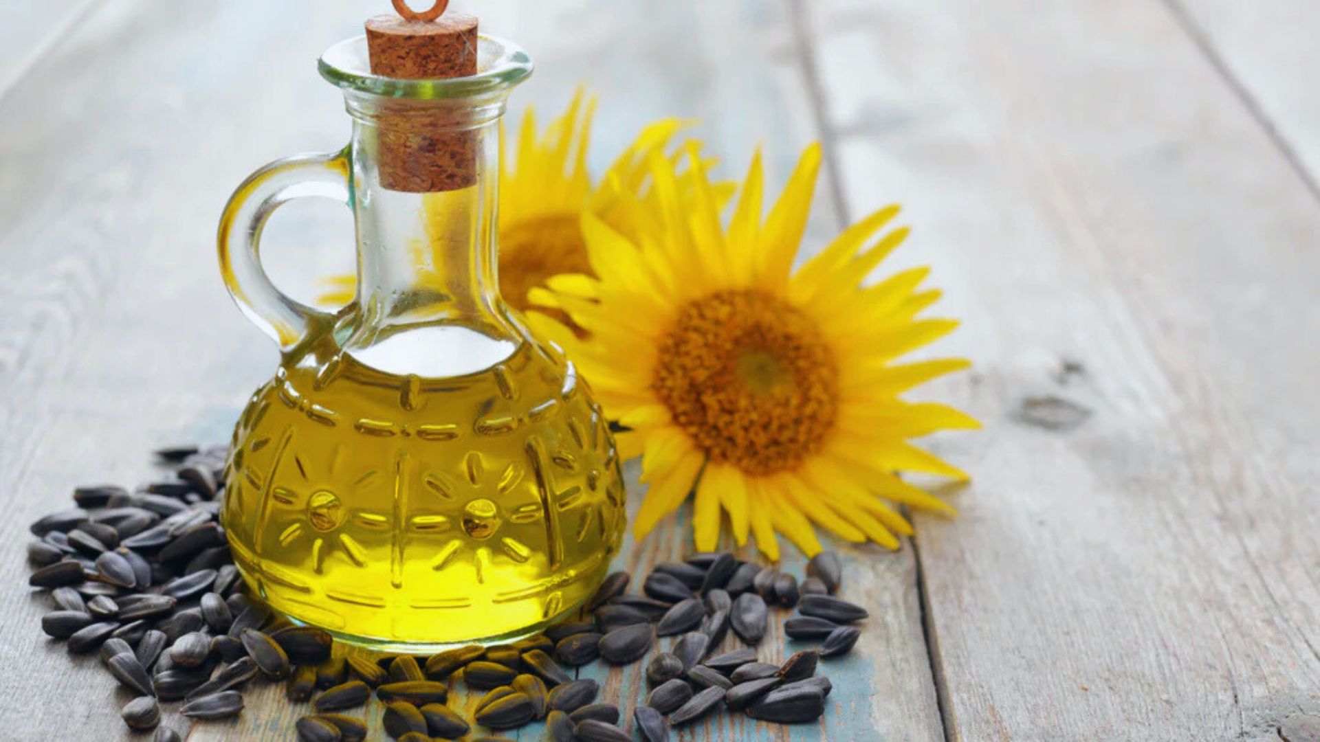 A bottle of sunflower oil next to a pile of sunflower seeds on a wooden surface.
