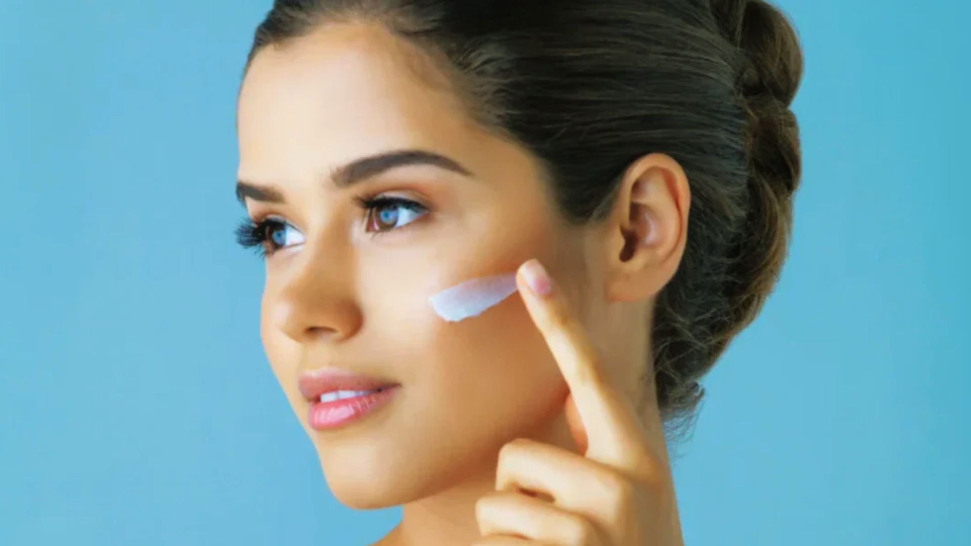 A woman gently applying cream to her face, focusing on skincare in a well-lit bathroom setting.