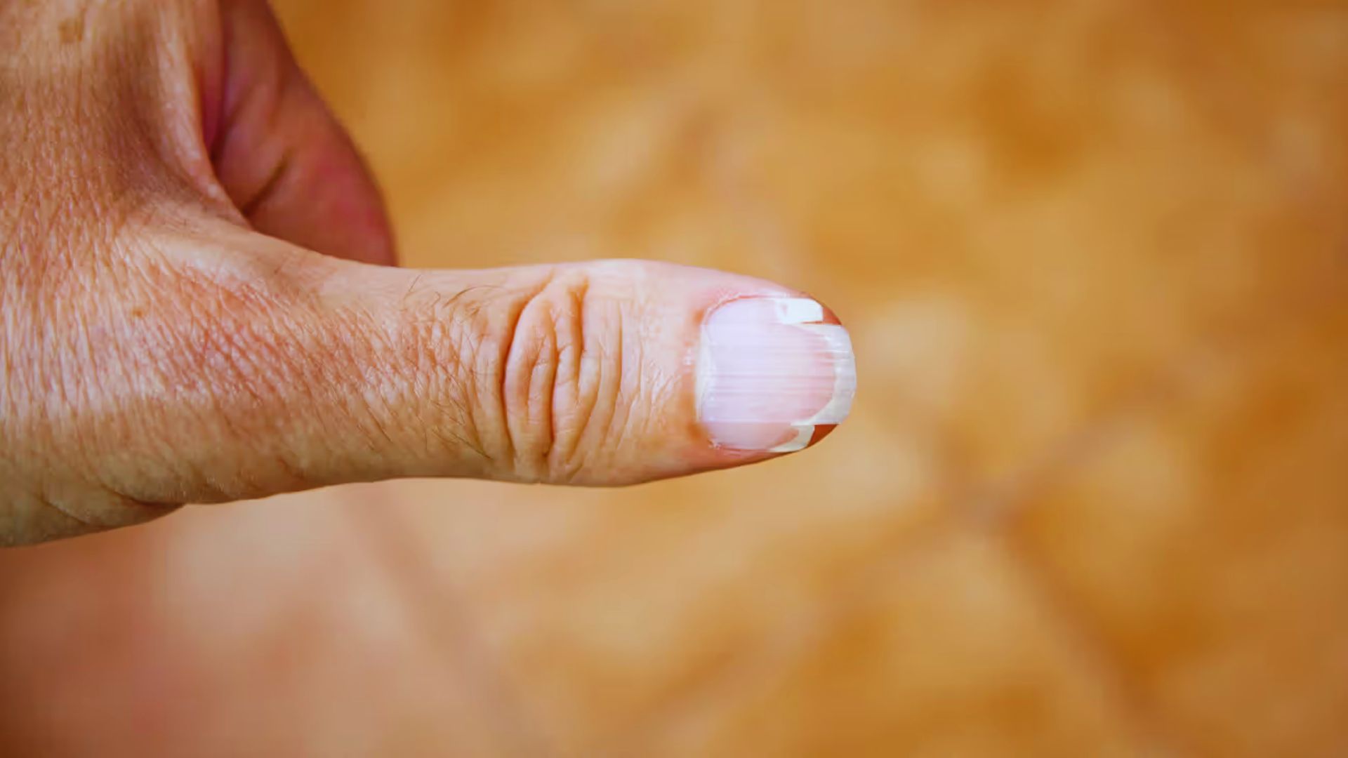A close-up of a finger displaying a neatly manicured white nail against a neutral background.