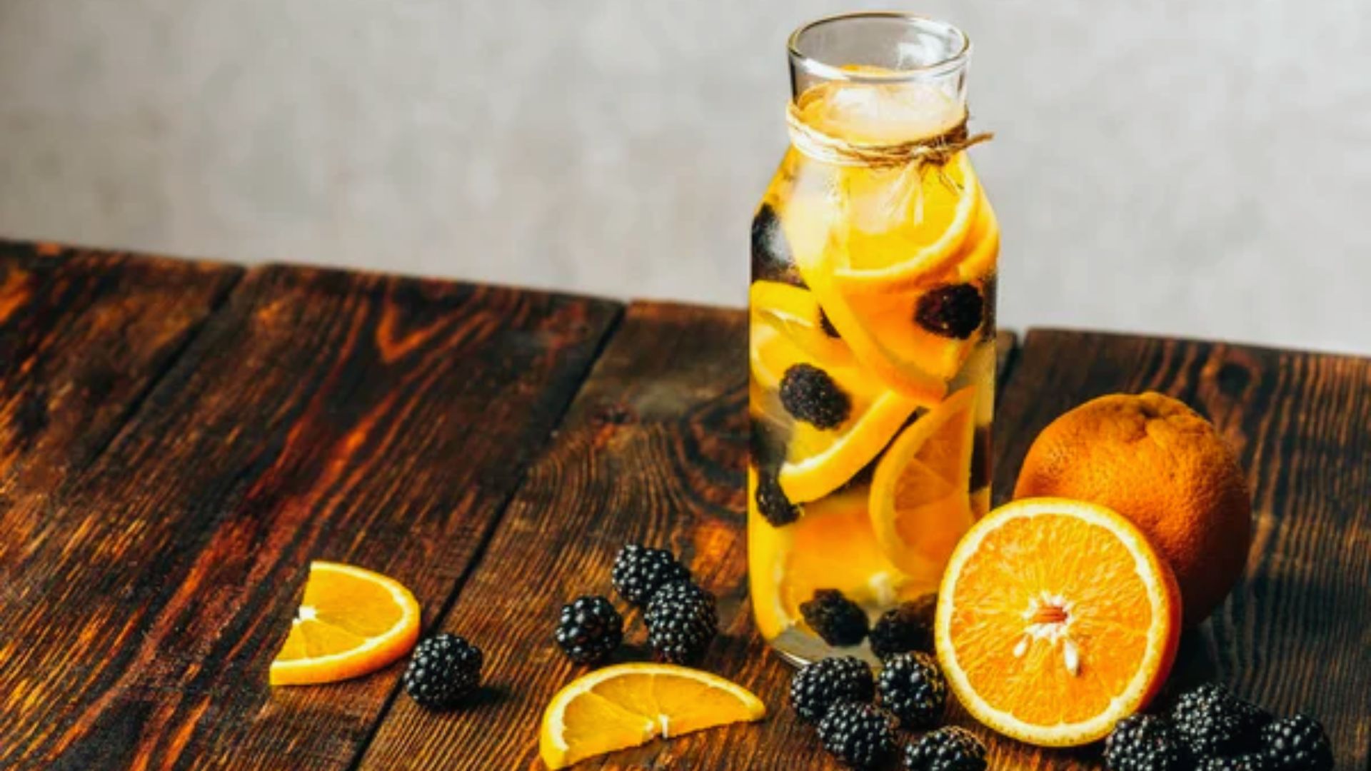 A glass bottle filled with orange slices and blackberries, showcasing vibrant fruit colors against a clear background.