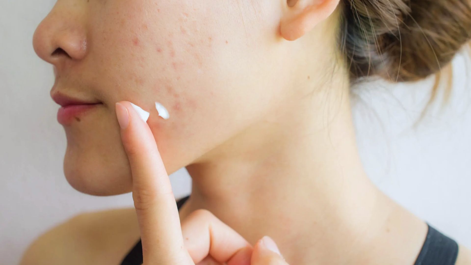 A woman applies cream to her skin, focusing on moisturizing and caring for her complexion.
