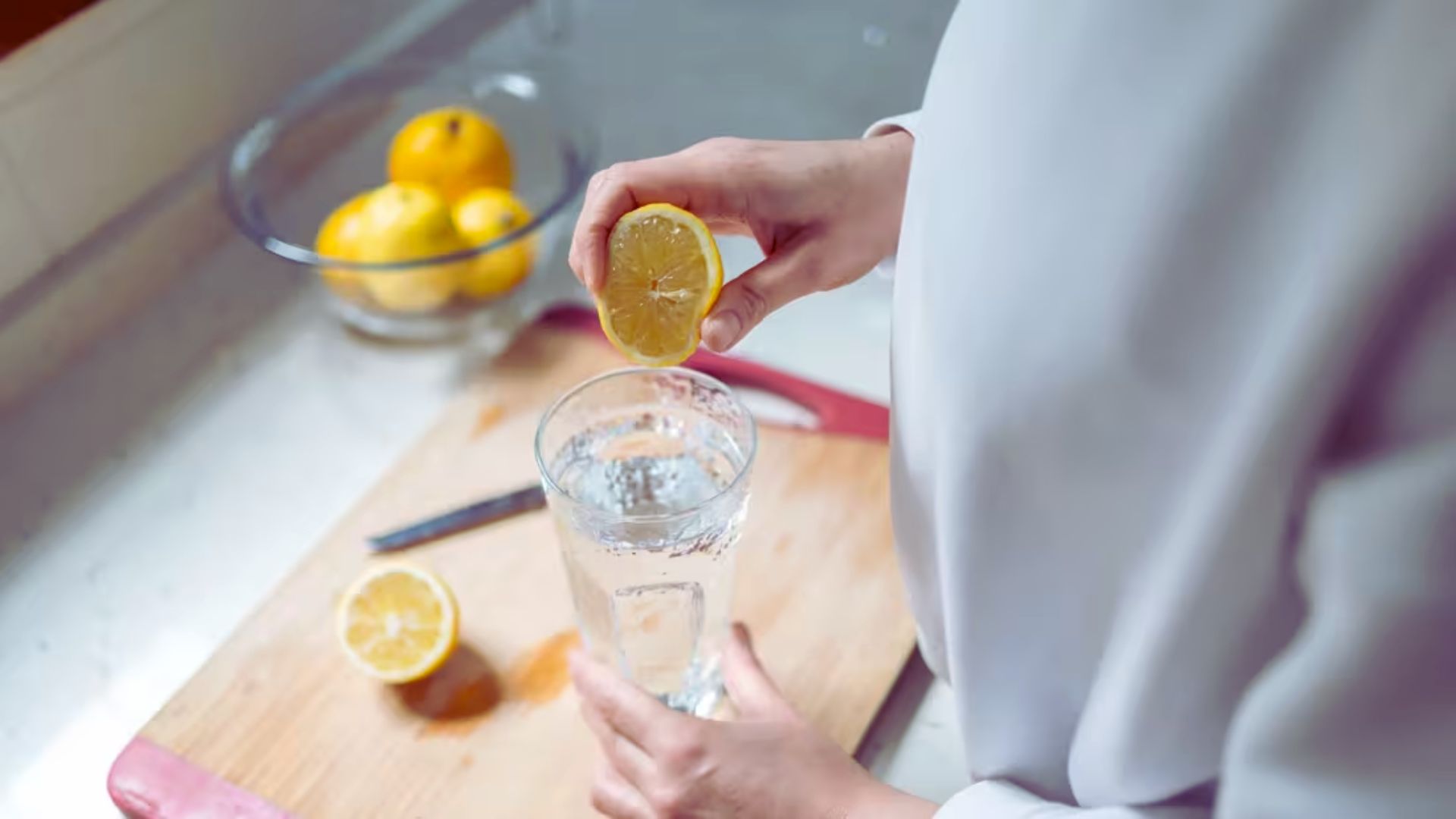 A person holds a lemon slice above a glass, showcasing a refreshing drink with citrus garnish.