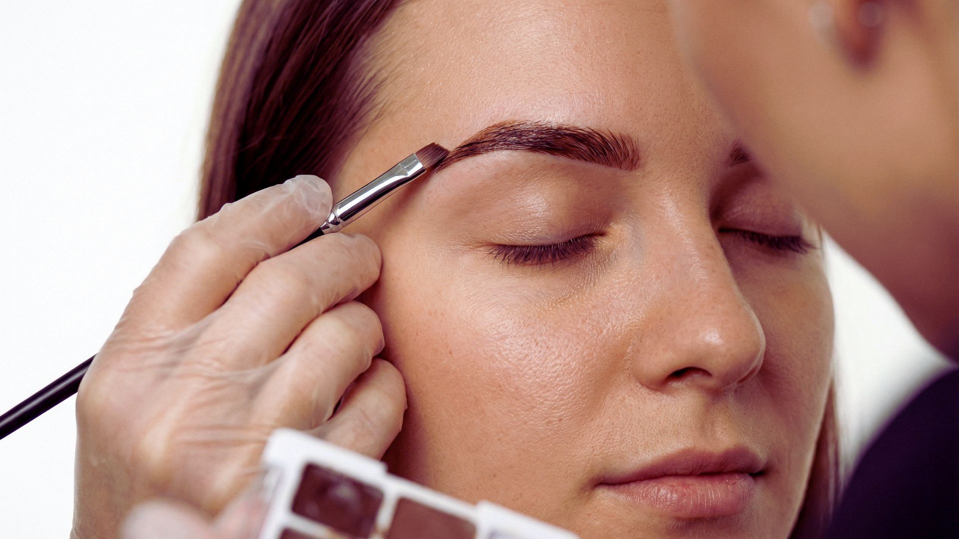 A woman receiving eyebrow shaping from a professional in a beauty salon setting.
