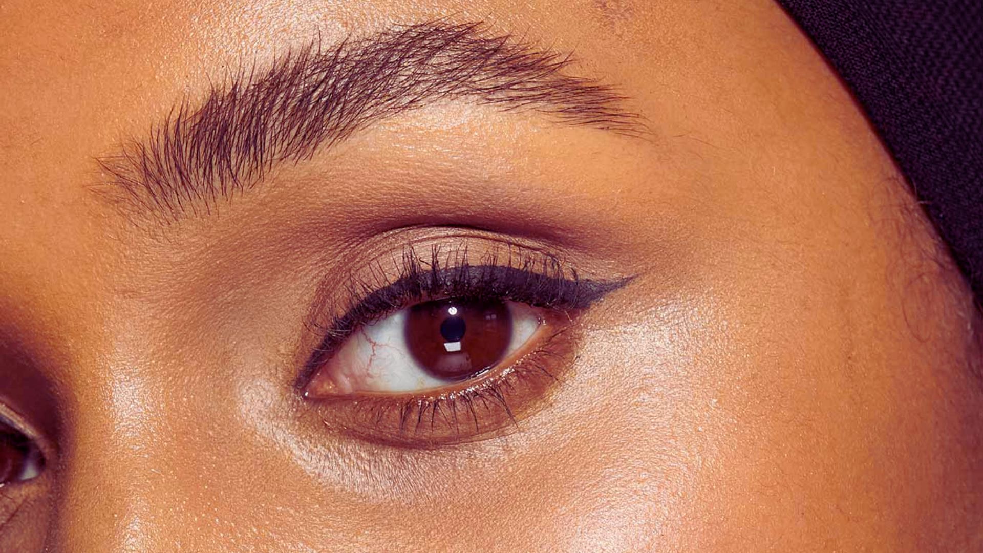 A woman's eye in close-up, framed by a black headscarf, emphasizing her expression and the intricate details of the scarf.