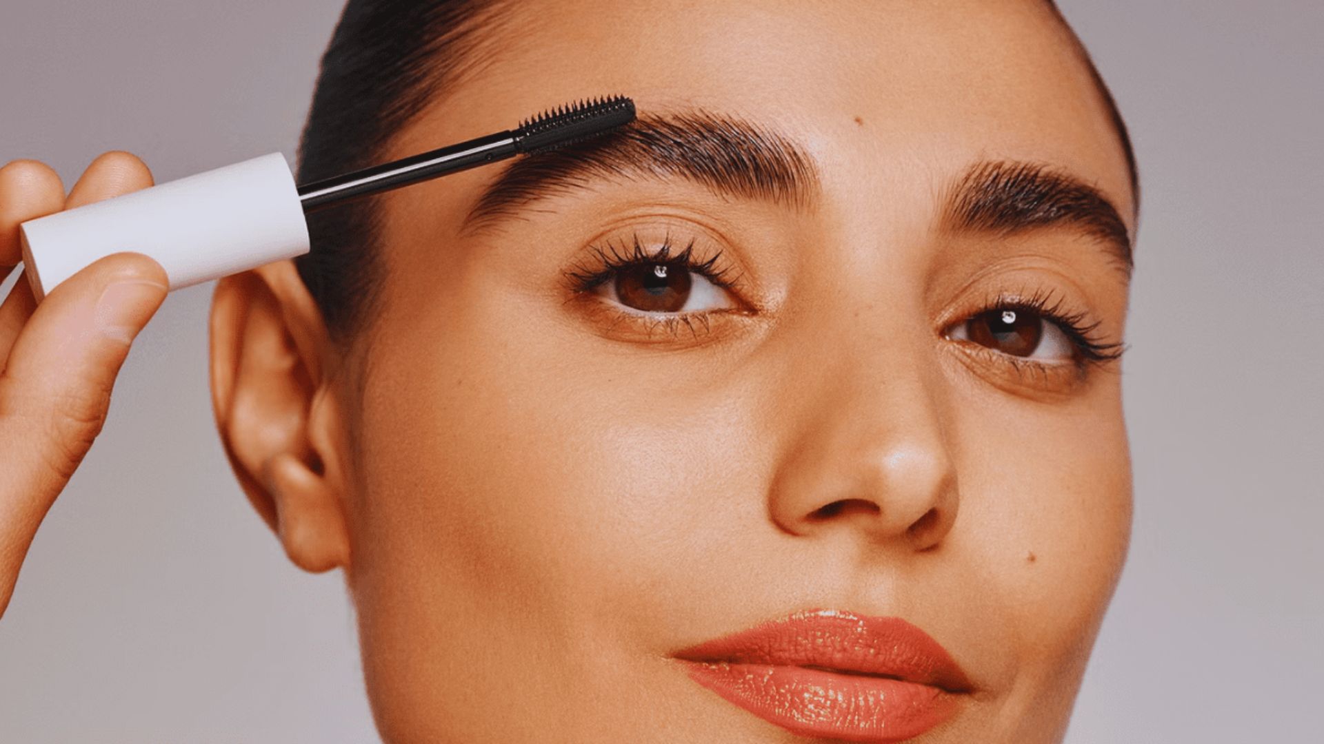 A woman carefully applies eyebrow makeup with a brush, focusing on achieving a polished look.