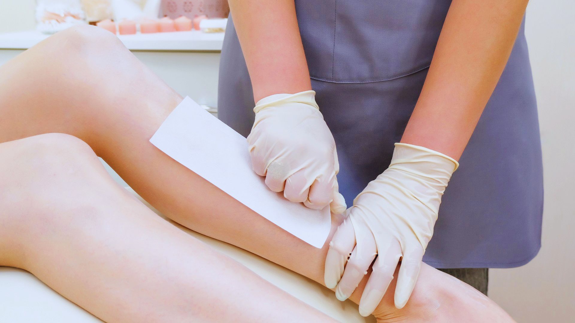 A woman is seated, receiving a leg waxing treatment at a beauty salon.