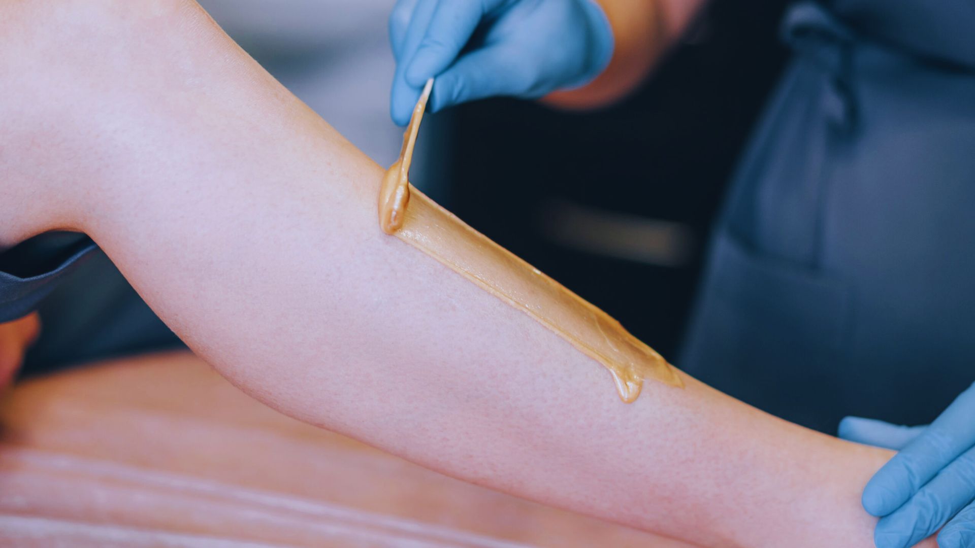 A person receiving a leg wax treatment in a salon, with a beautician applying wax to their skin.