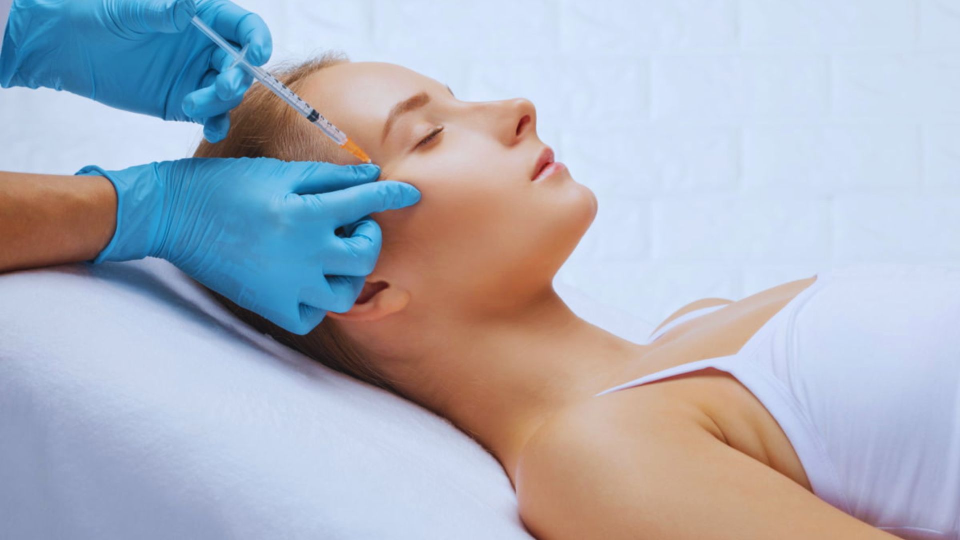 A woman receiving a facial injection in a clinical setting, focusing on her expression and the procedure being performed.