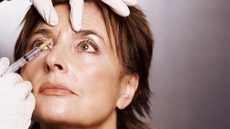 A woman receiving a facial injection in a clinical setting, focused on her expression during the procedure.