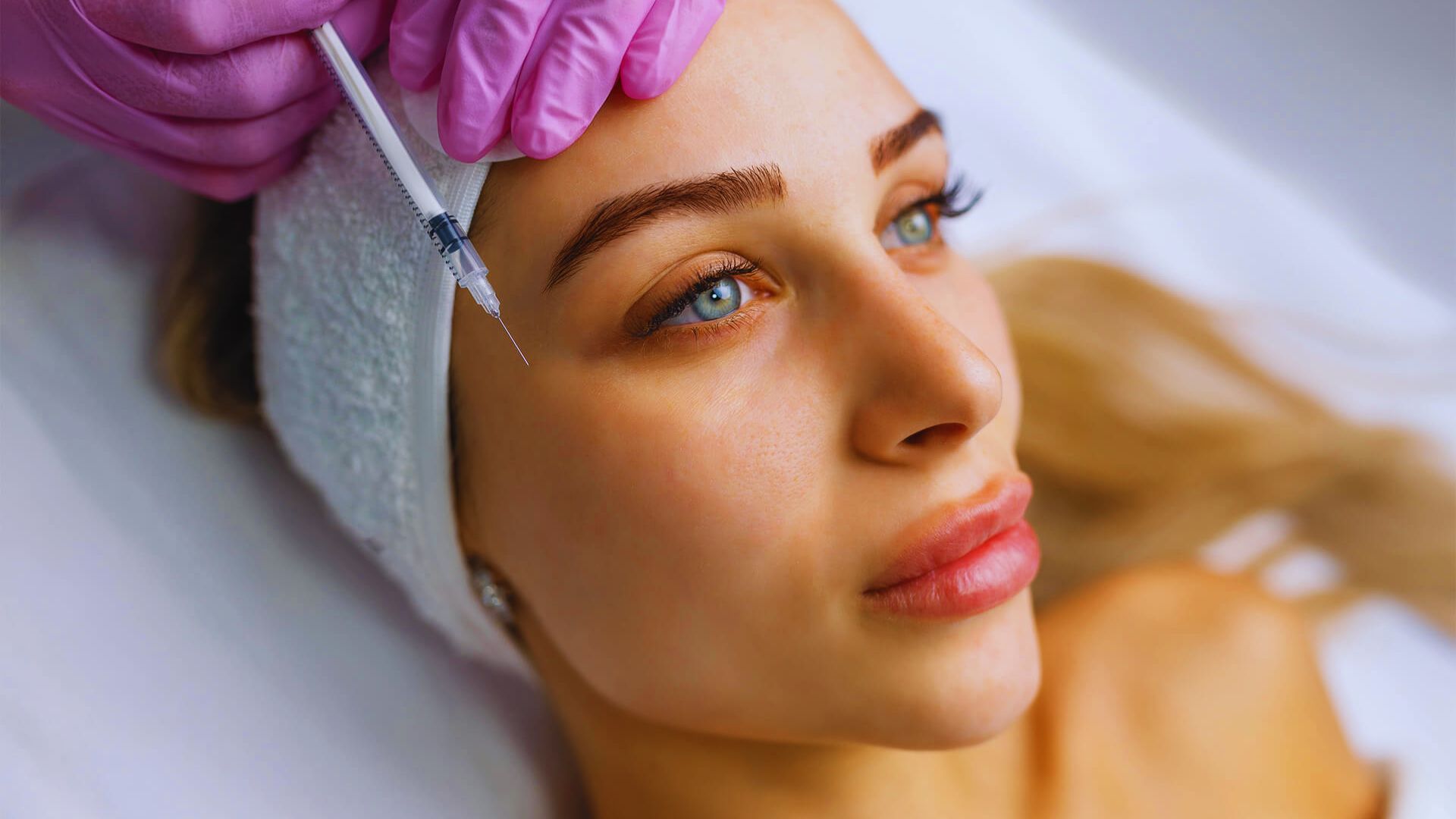 A woman receiving a facial treatment, relaxing on a spa bed with a serene expression and a therapist applying products.