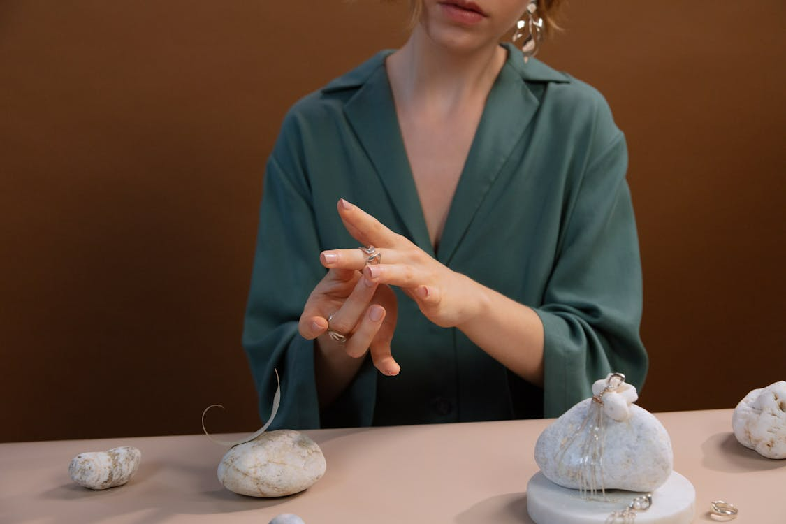 A woman seated at a table, surrounded by white rocks, appears deep in thought or contemplation.