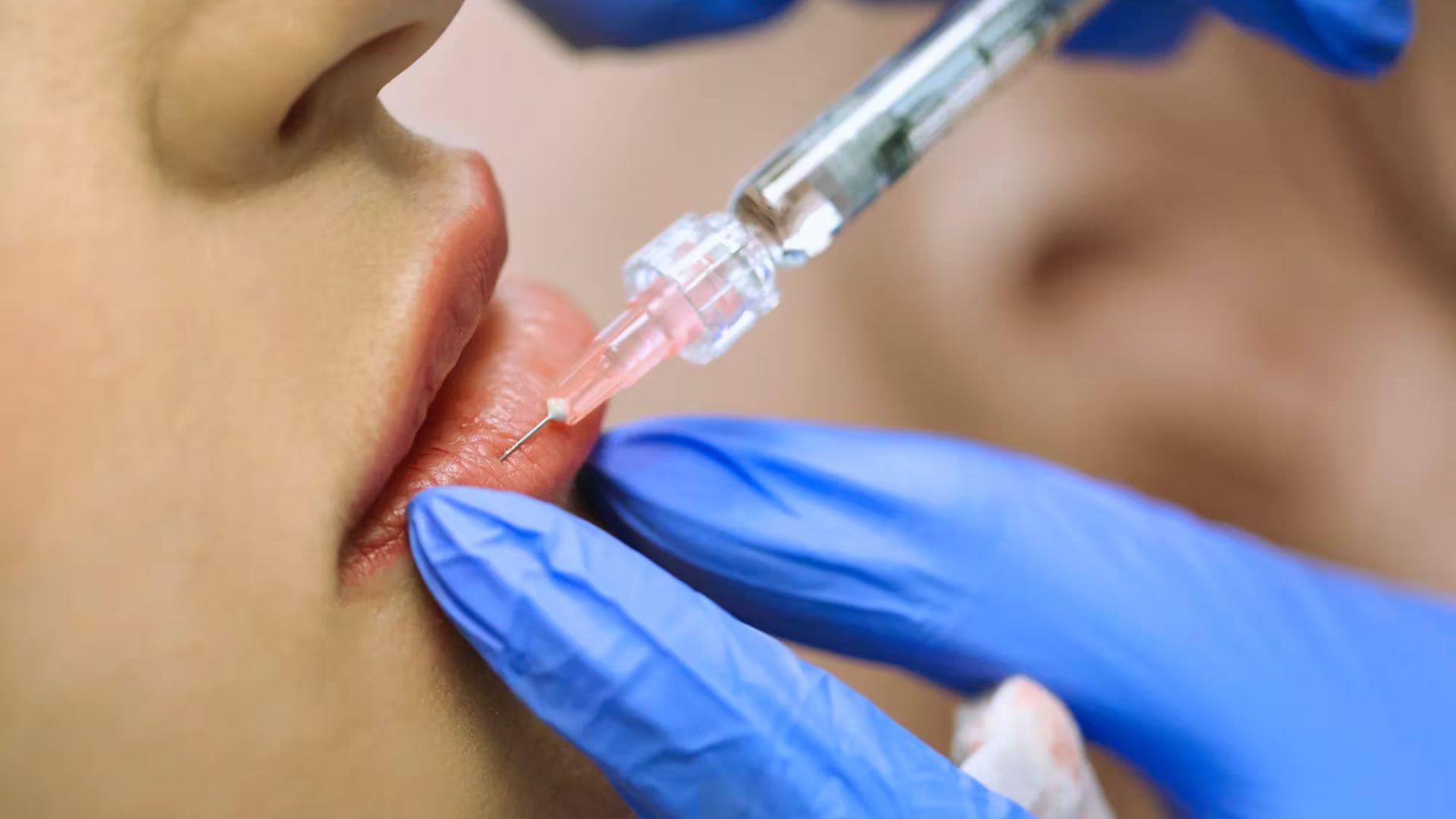 Close-up of lips receiving an injection from a syringe held by gloved hands, suggesting a cosmetic procedure. The atmosphere is clinical and precise.