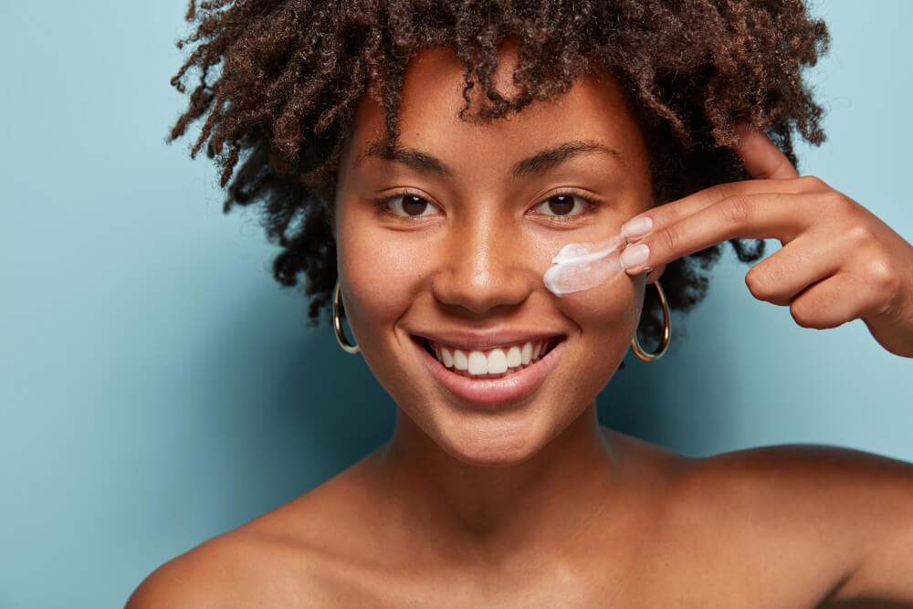 A smiling woman with curly hair holds a cream, showcasing a joyful expression and a sense of warmth.