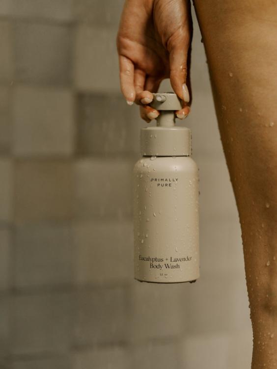 A woman stands in front of a shower, holding a bottle of water, ready for a refreshing rinse.