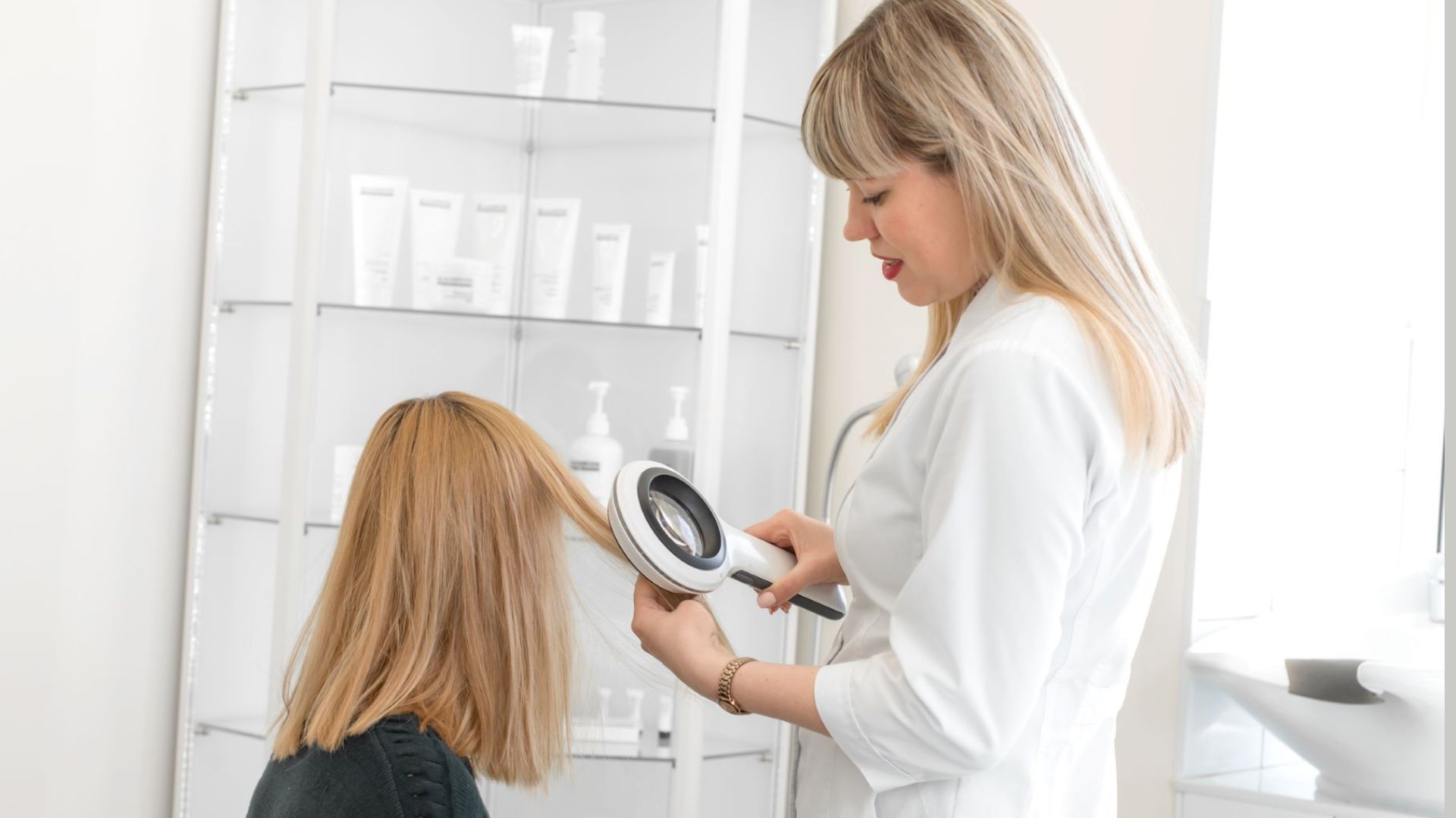 A dermatologist examines a patient’s hair with a magnifying tool in a bright clinic. Shelves with hair care products are visible in the background.
