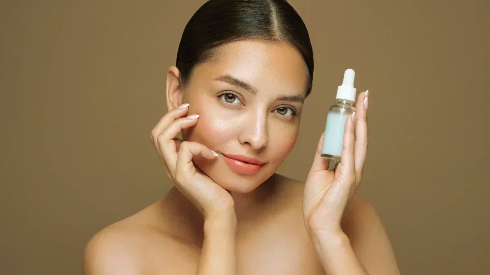 Woman with smooth skin holds a serum bottle, smiling softly. She is against a beige background, exuding a calm, elegant, and fresh tone.