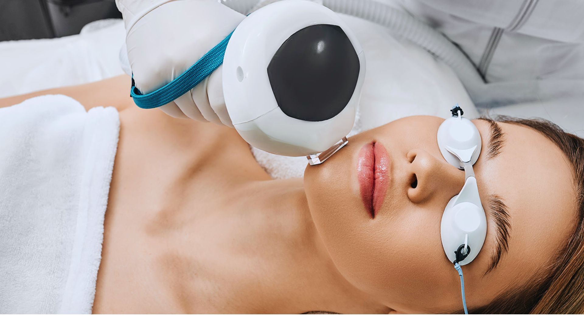 A woman lying down receives a laser facial treatment while wearing protective goggles. The atmosphere is calm, emphasizing skincare and relaxation.