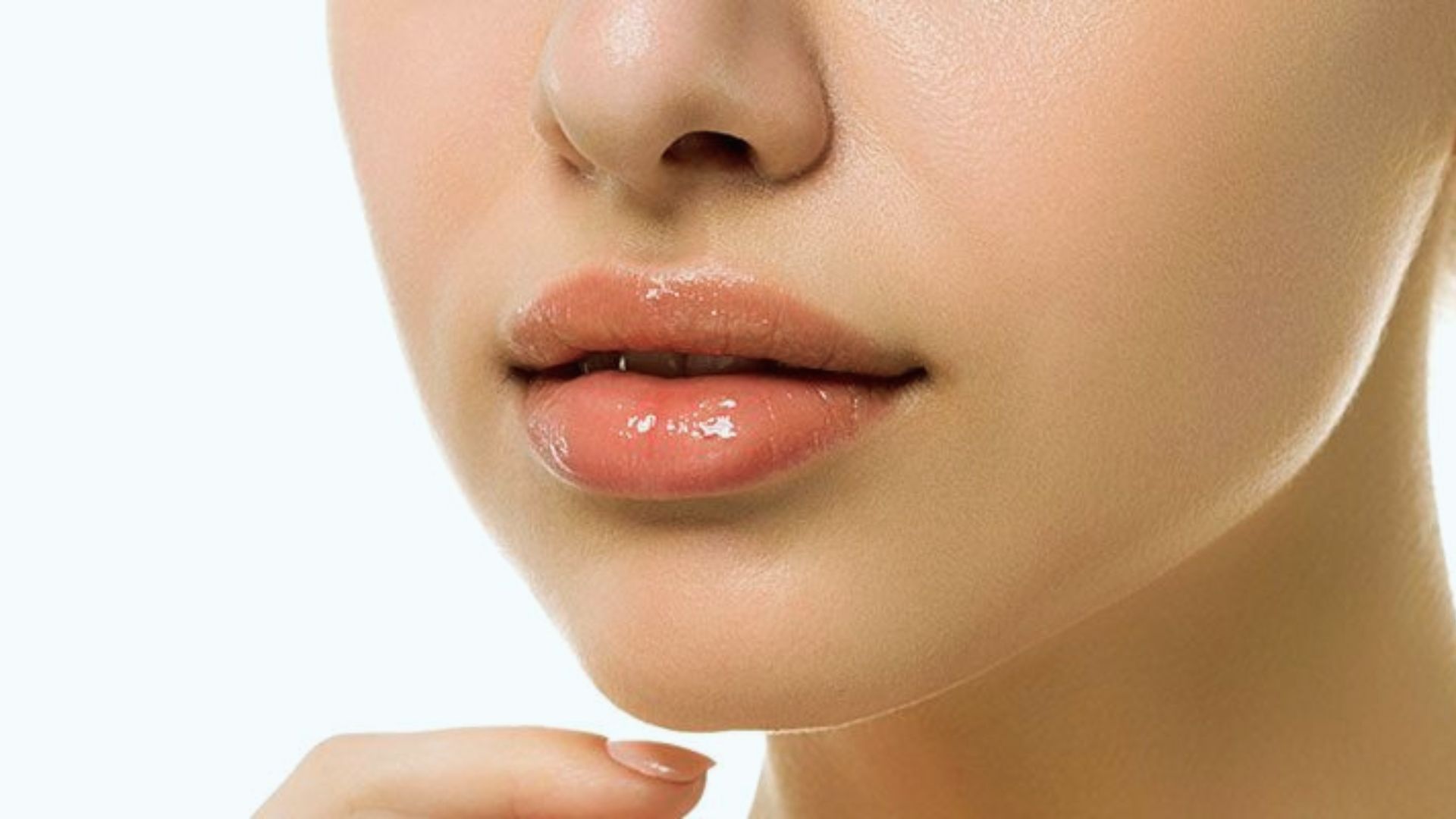 Close-up of a person’s glossy, pink lips and smooth chin, with a finger gently touching. The skin appears clear and moisturized, conveying a fresh and polished tone.