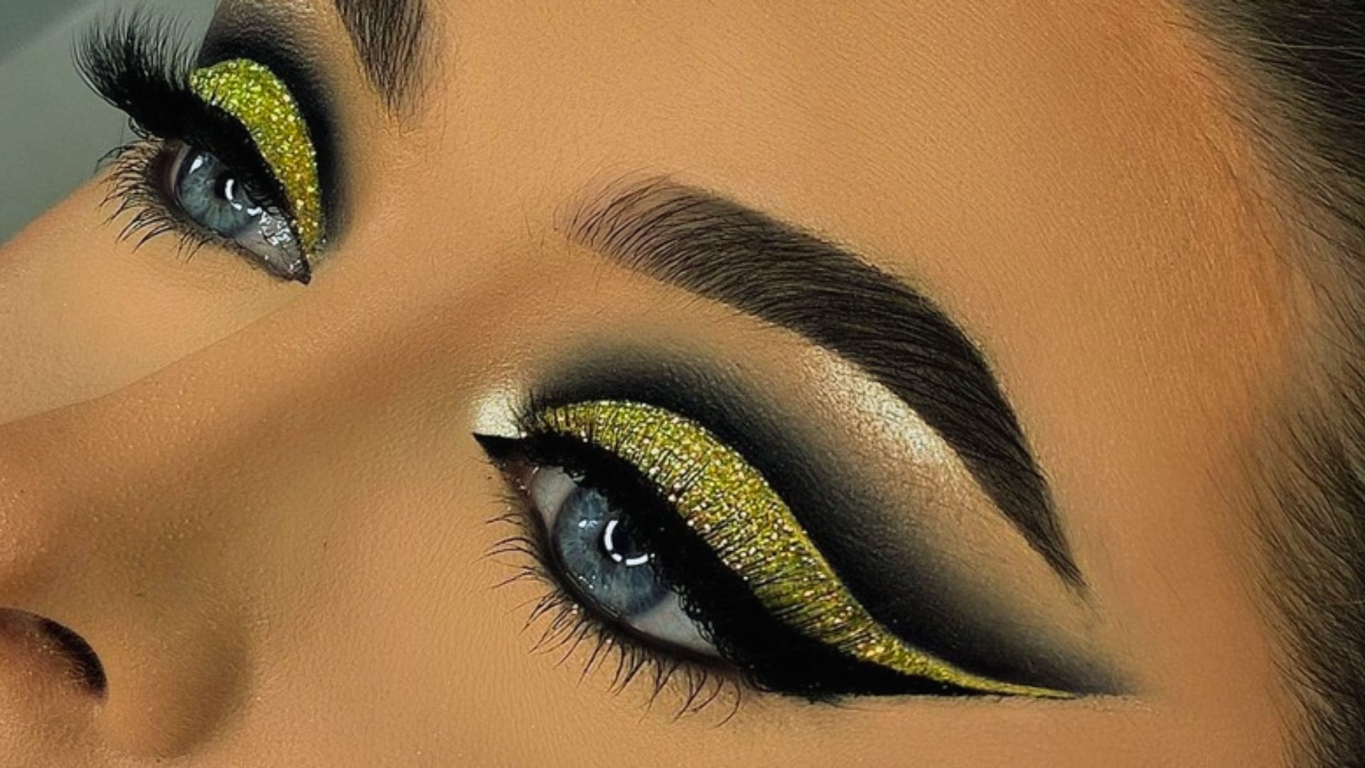 Close-up of eyes with dramatic makeup: glittery gold eyeshadow, bold black eyeliner, and thick lashes. The look is glamorous and striking.