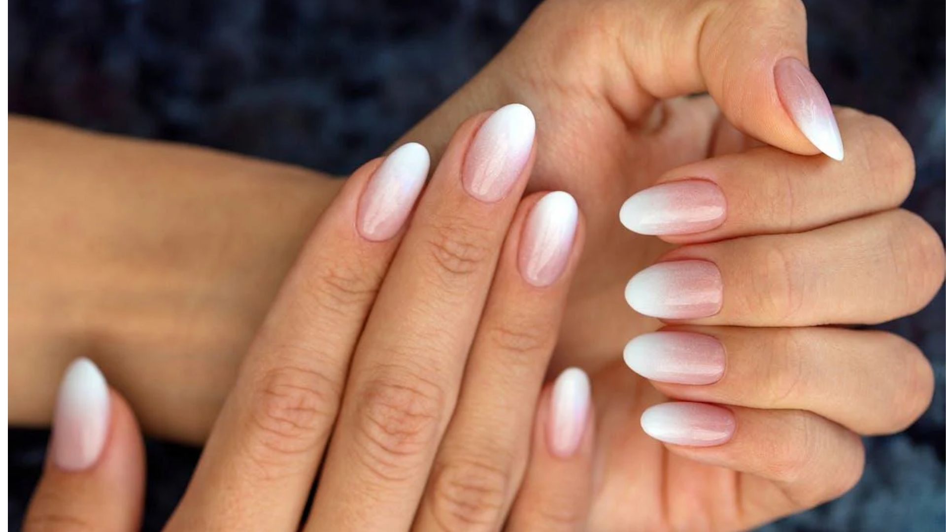 Close-up of hands displaying nails with a pink and white ombre manicure. The nails are oval-shaped, creating a stylish and elegant look.