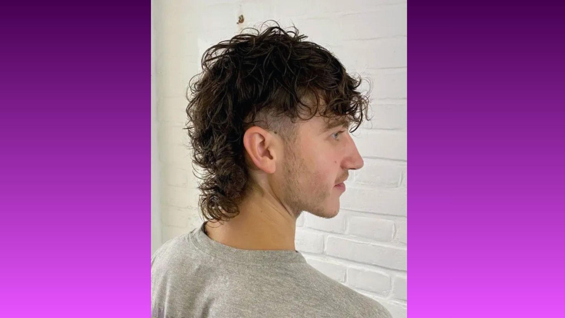 Young man with curly dark mullet hairstyle facing sideways, standing against a white brick wall. The vibe is trendy and bold, with a purple gradient background.