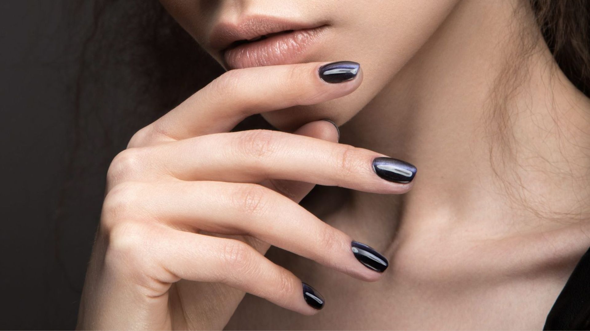 Close-up of a woman softly touching her lips with her fingers, showcasing glossy black nail polish. The mood is elegant and reflective.