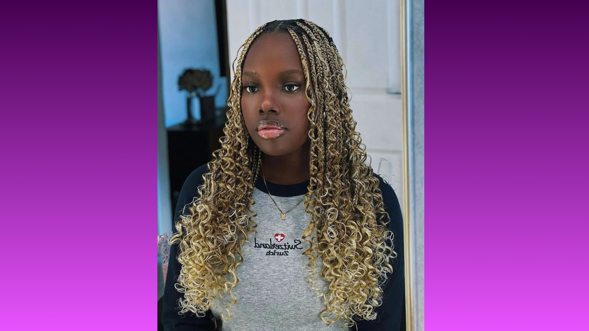 Young woman with long, curly, blonde braids wears a gray sweater with text, set against a purple gradient background, conveying a confident and trendy vibe.