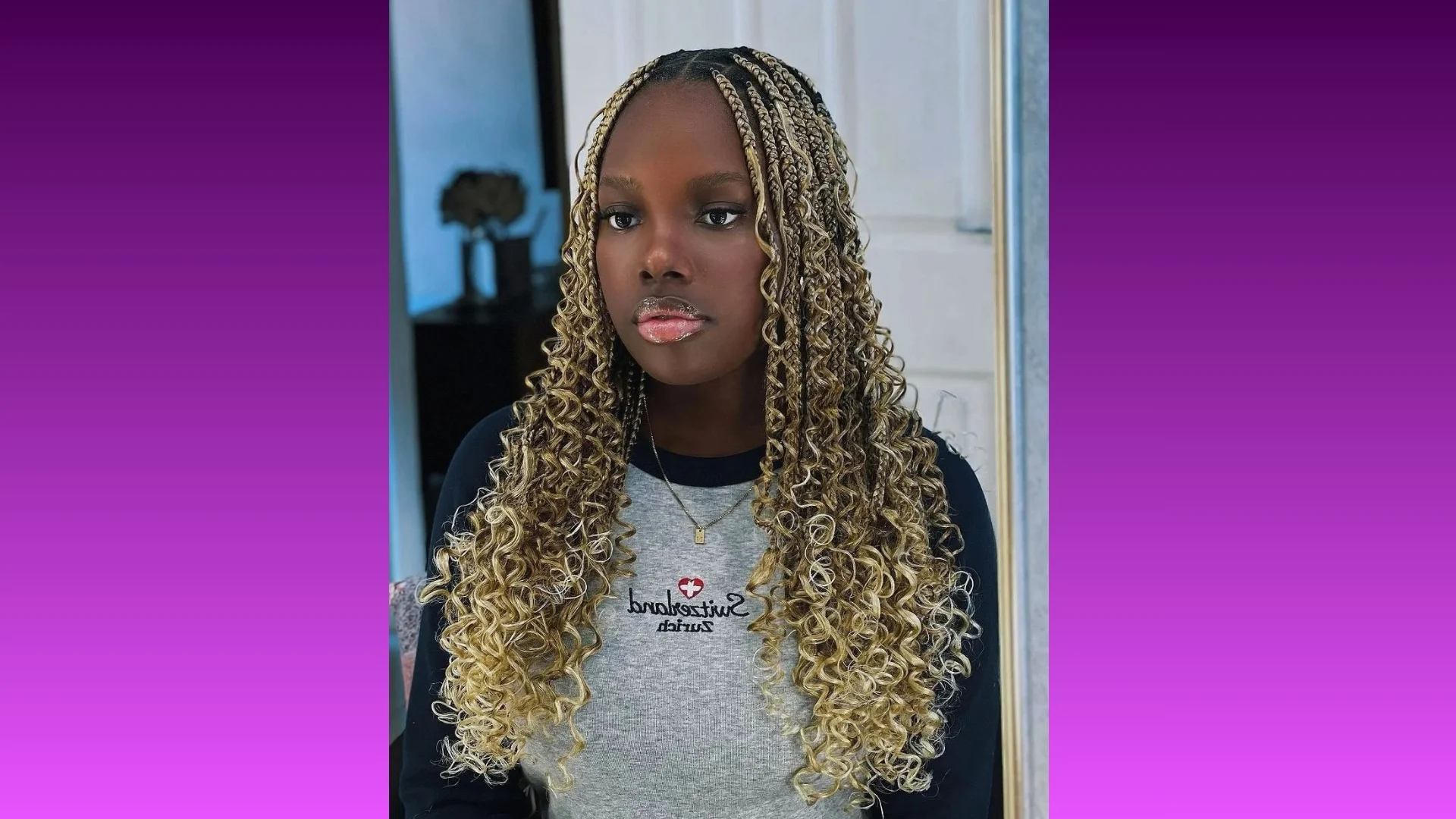 Young woman with long, curly, blonde braids wears a gray sweater with text, set against a purple gradient background, conveying a confident and trendy vibe.