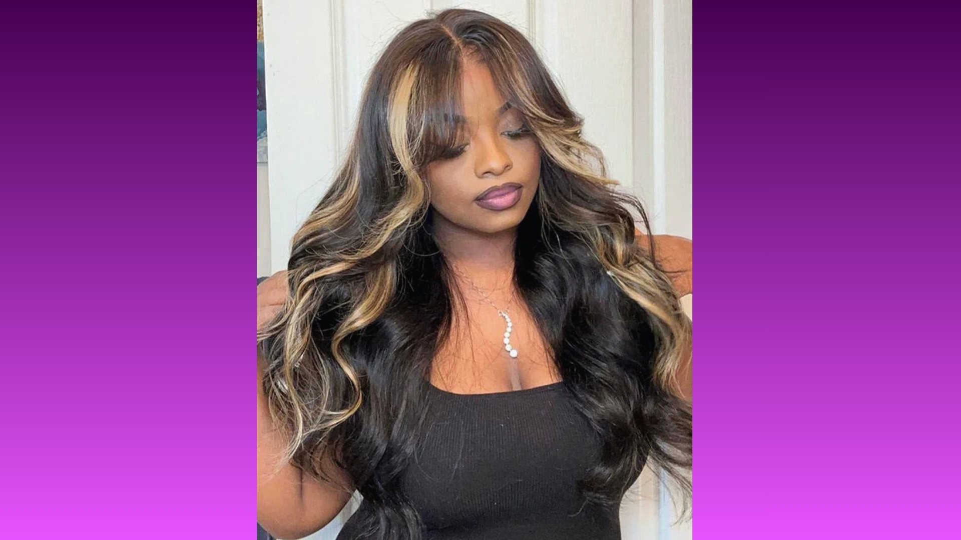 Woman with long, wavy hair featuring blonde highlights stands against a purple background. Her expression is calm and confident, wearing a black top.