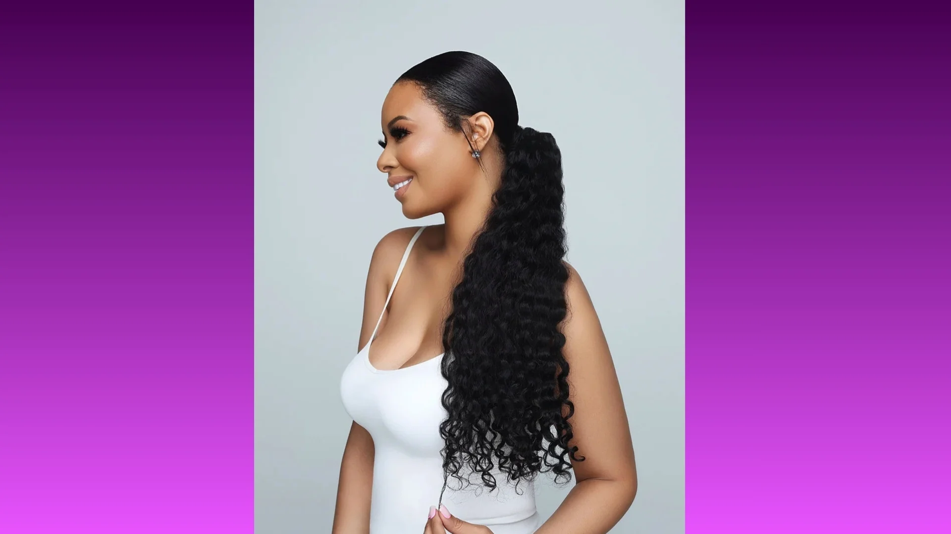A woman with long, curly black hair tied in a ponytail smiles in profile against a gradient purple background, wearing a white tank top.