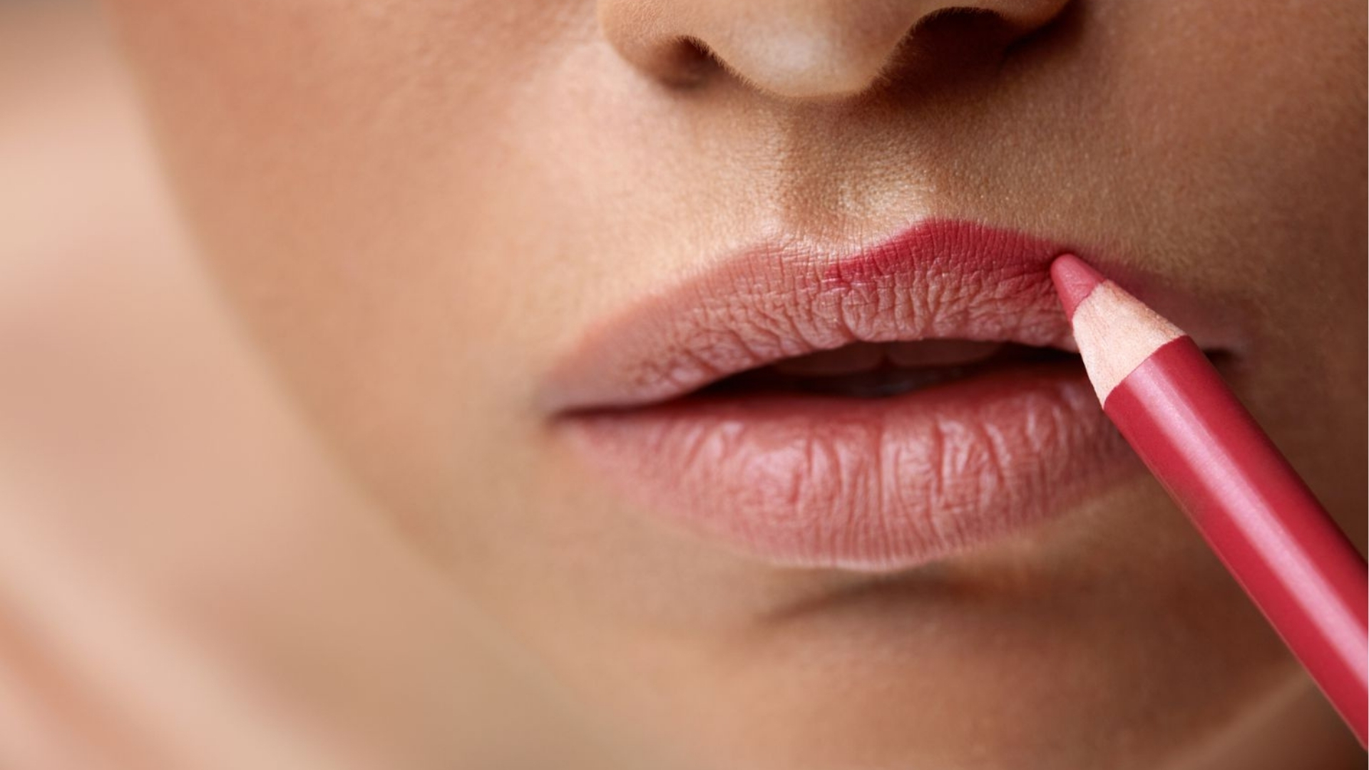 Close-up of a person applying pink lip liner to their lips, highlighting a precise, defined application. The image conveys a focus on beauty and care.