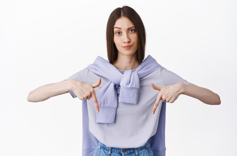 A woman in a blue shirt and jeans holds up two fingers in a peace sign gesture.