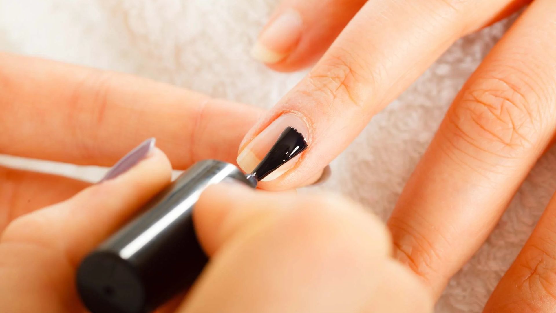 Close-up of a hand receiving a manicure. A person is applying black nail polish to a fingernail with a brush, conveying a sense of care and precision.