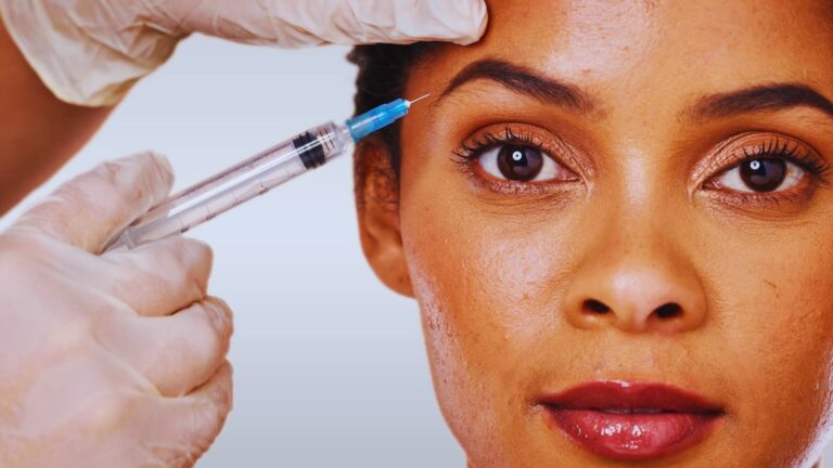 A woman receives a cosmetic injection near her eyebrow. A gloved hand holds the syringe. The expression is calm, indicating trust and confidence.